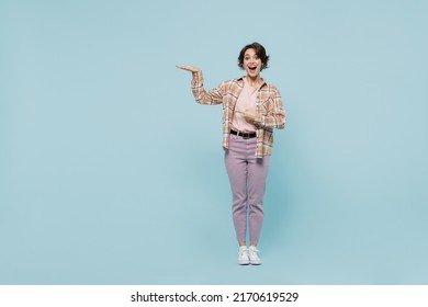 Full body young smiling excited happy woman 20s wearing casual brown shirt point hands show height scale isolated on pastel plain light blue color background studio portrait. People lifestyle concept