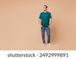 Full body young smiling fun happy cheerful middle eastern man wear blue t-shirt casual clothes look aside on area mock up isolated on plain pastel beige background studio portrait. Lifestyle concept