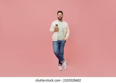 Full Body Young Smiling Happy Man 20s In Trendy Jacket Shirt Hold Takeaway Delivery Craft Paper Brown Cup Coffee To Go Isolated On Plain Pastel Light Pink Background Studio. People Lifestyle Concept