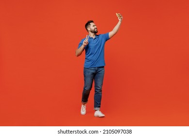 Full Body Young Smiling Happy Caucasian Man 20s Wear Basic Blue T-shirt Do Selfie Shot On Mobile Cell Phone Show V-sign Isolated On Plain Orange Background Studio Portrait. People Lifestyle Concept