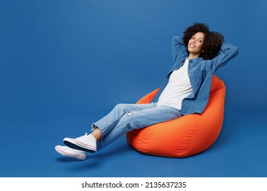 Full Body Young Smiling Happy Black Woman In Casual Clothes Shirt White T-shirt Sit In Bag Chair Hold Hands Behind Neck Relax Isolated On Plain Dark Blue Background Studio. People Lifestyle Concept