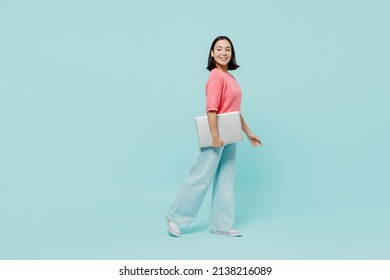 Full Body Young Smiling Happy Woman Of Asian Ethnicity 20s In Pink Sweater Hold Closed Laptop Pc Computer Walk Go Isolated On Pastel Plain Light Blue Color Background Studio. People Lifestyle Concept