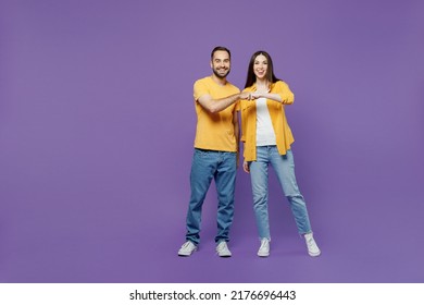 Full body young smiling happy couple two friends family man woman together in yellow casual clothes looking camera giving fist bump in agreement isolated plain violet background studio portrait