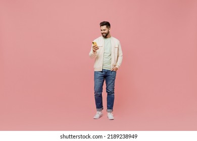 Full body young smiling happy caucasian man 20s wearing trendy jacket shirt hold in hand use mobile cell phone isolated on plain pastel light pink background studio portrait. People lifestyle concept - Shutterstock ID 2189238949