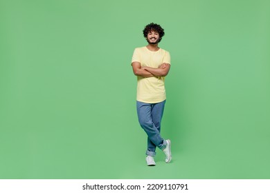 Full Body Young Smiling Happy Indian Man 20s In Basic Yellow T-shirt Hold Hands Crossed Folded Look Camera Isolated On Plain Pastel Light Green Background Studio Portrait. People Lifestyle Concept.