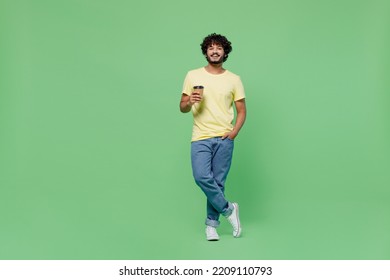 Full body young smiling happy Indian man 20s in basic yellow t-shirt hold takeaway delivery craft paper brown cup coffee to go isolated on plain pastel light green background. People lifestyle concept - Powered by Shutterstock