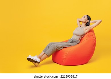 Full Body Young Smiling Happy Fun Cool Latin Woman 30s She Wear Basic Beige Tank Shirt Sit In Bag Chair Hold Hands Behind Neck Isolated On Plain Yellow Color Backround Studio People Lifestyle Concept