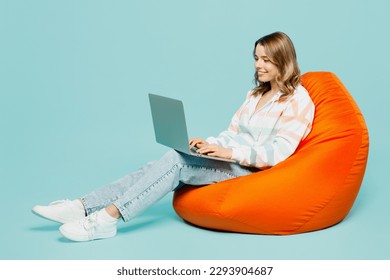 Full body young IT smiling happy woman wear striped hoody sit in bag chair hold use work on laptop pc computer isolated on plain pastel light blue cyan background studio portrait. Lifestyle concept - Powered by Shutterstock