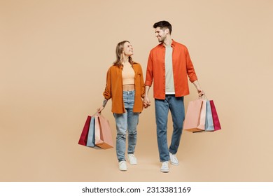 Full body young smiling happy couple two friends family man woman wears casual clothes hold shopping paper package bags together isolated on plain beige background. Black Friday sale buy day concept - Powered by Shutterstock