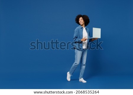 Full body young smiling happy black woman in casual clothes shirt white t-shirt hold use work on laptop pc computer look aside isolated on plain dark blue background studio. People lifestyle concept