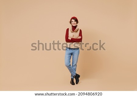 Full body young smiling happy fun attractive cheerful caucasian woman 20s in red turtleneck yellow vest beret hold hands crossed folded isolated on plain pastel beige color background studio portrait