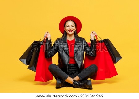 Full body young smiling happy cheerful woman wears casual clothes red hat sitting hold shopping paper package bags look camera isolated on plain yellow background. Black Friday sale buy day concept