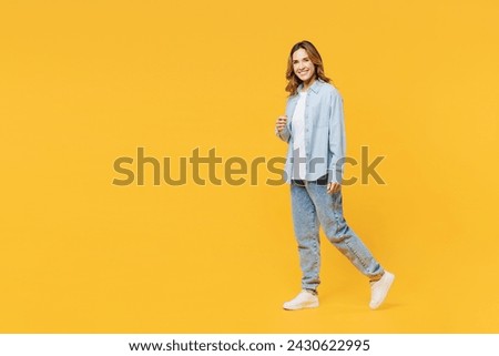 Full body young smiling happy fun cheerful woman she wear blue shirt white t-shirt casual clothes walking going looking camera isolated on plain yellow background studio portrait. Lifestyle concept