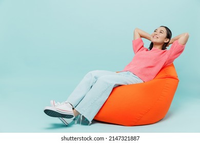 Full body young smiling minded fun woman of Asian ethnicity 20s wear pink sweater sit in bag chair hold hands behind neck isolated on pastel plain light blue color background People lifestyle concept - Powered by Shutterstock