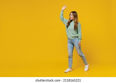 Full Body Young Smiling Satisfied Happy Fun Woman 30s Wearing Green Knitted Sweater Walk Go Strolling Waving Hand Isolated On Plain Yellow Color Background Studio Portrait. People Lifestyle Concept