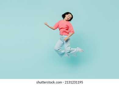 Full body young smiling singer happy woman of Asian ethnicity 20s in pink sweater jump high paly guitar isolated on pastel plain light blue color background studio portrait. People lifestyle concept