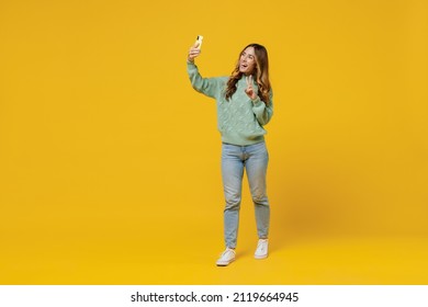 Full Body Young Smiling Woman 30s Wearing Green Knitted Sweater Doing Selfie Shot On Mobile Cell Phone Show V-sign Isolated On Plain Yellow Color Background Studio Portrait. People Lifestyle Concept