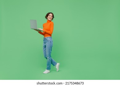 Full Body Young Smiling Woman 20s Wear Casual Orange Turtleneck Hold Use Work On Laptop Pc Computer Look Aside Walk Go Isolated On Plain Pastel Light Green Color Background. People Lifestyle Concept