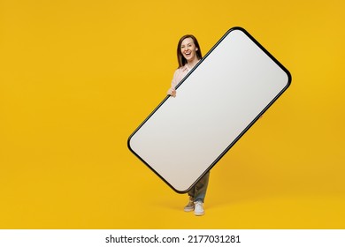 Full body young smiling woman she in striped shirt white t-shirt hold big huge blank screen mobile cell phone with workspace copy space mockup area show thumb up isolated on plain yellow background - Shutterstock ID 2177031281