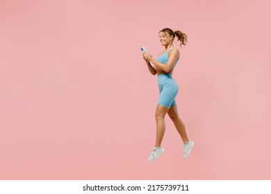 Full body young sporty athletic fitness trainer woman wears blue tracksuit spend time in home gym jump high use mobile cell phone isolated on pastel plain light pink background. Workout sport concept - Powered by Shutterstock