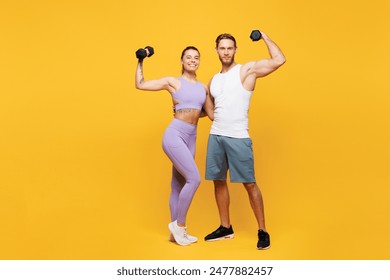 Full body young young strong fitness trainer instructor sporty two man woman wear blue clothes spend time in home gym hold in hand dumbbells isolated on plain yellow background. Workout sport concept - Powered by Shutterstock