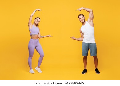 Full body young strong fitness trainer sporty two man woman wear blue clothes spend time in home gym point finger on area between them isolated on plain yellow background. Workout sport fit concept - Powered by Shutterstock