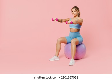 Full body young strong sporty athletic fitness trainer instructor woman wear blue tracksuit spend time in home gym sit on fitball isolated on pastel plain light pink background. Workout sport concept