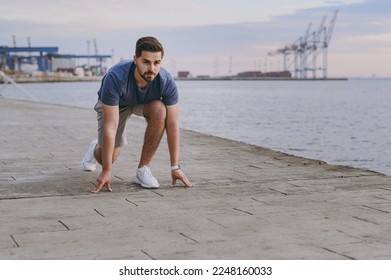 Full body young strong sporty toned fit sportsman man wear sports clothes warm up training stand at low start going to run at sunrise sun over sea beach outdoor on pier seaside in summer day morning. - Powered by Shutterstock