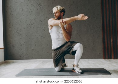 Full body young strong sporty athletic sportsman man wear white tank shirt black shorts training doing stretch lunge exercise for hands look aside warm up training indoor at gym. Workout sport concept - Powered by Shutterstock