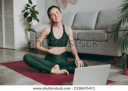 Full body young strong sporty athletic fitness trainer instructor woman wear green tracksuit use laptop pc computer put hand on belly train do exercises at home gym Workout sport motivation concept