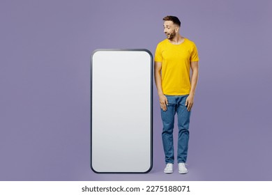 Full body young surprised shocked amazed impressed fun man wear yellow t-shirt looking at big huge blank screen mobile cell phone smartphone with area isolated on plain pastel light purple background - Powered by Shutterstock