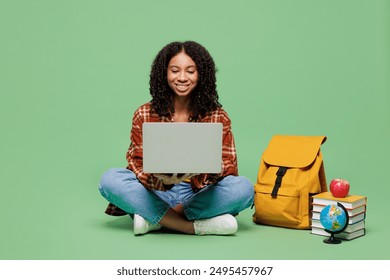 Full body young teen girl IT student wear brown yellow casual clothes sits near backpack bag books hold use laptop pc computer isolated on plain green background High school university college concept - Powered by Shutterstock