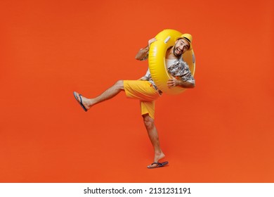 Full body young tourist man wear beach shirt hat hold inflatable ring lean back raise up leg fooling around isolated on plain orange background studio portrait Summer vacation sea rest sun tan concept - Shutterstock ID 2131231191