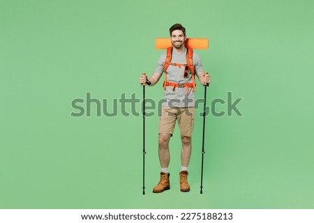Full body young traveler white man carry backpack stuff mat walk with trakking poles isolated on plain green background. Tourist leads active healthy lifestyle. Hiking trek rest travel trip concept
