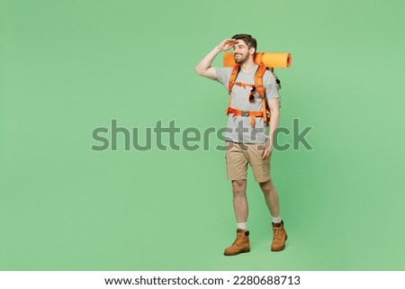 Full body young traveler white man carry backpack stuff mat walk look far away distance isolated on plain green background. Tourist leads active healthy lifestyle. Hiking trek rest travel trip concept