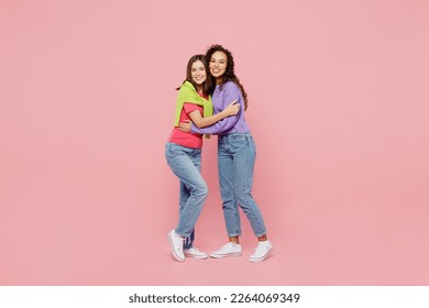 Full body young two friends smiling happy fun cool cheerful positive women 20s wear green purple shirts together stand look camera hug homie isolated on pastel plain light pink color background studio