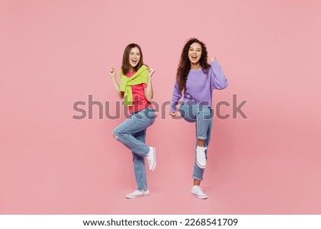 Full body young two friends overjoyed happy fun cool cheerful smiling women 20s wear green purple shirts together do winner gesture raise up leg isolated on pastel plain light pink color background