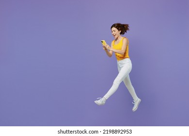 Full Body Young Woman 20s Wear Yellow Tank Shirt Jump High Run Fast Hold In Hand Use Mobile Cell Phone Device Isolated On Plain Pastel Light Purple Background Studio Portrait. People Lifestyle Concept