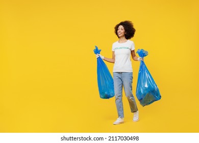 Full Body Young Woman Of African American Ethnicity In White Volunteer T-shirt Carry Trash Bags After Rubbish Removing Isolated On Plain Yellow Background. Voluntary Free Work Assistance Help Concept