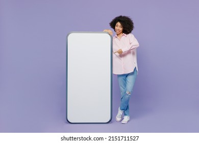 Full body young woman of African American ethnicity wear pink striped shirt point finger on mobile cell phone with blank screen workspace area show thumb up isolated on plain pastel purple background - Shutterstock ID 2151711527