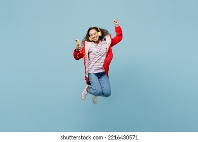 Full Body Young Woman Of African American Ethnicity 20s Wear Red Jacket Headphones Listen Music Jump High Use Mobile Cell Phone Do Winner Gesture Isolated On Plain Pastel Light Blue Cyan Background