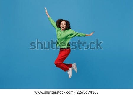Full body young woman of African American ethnicity 20s she wear green shirt jump high with outsretched hands like flying isolated on plain blue background studio portrait. People lifestyle concept