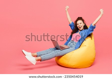 Full body young IT woman of African American ethnicity wears blue shirt casual clothes sit in bag chair hold use work on laptop pc computer do winner gesture isolated on plain pastel pink background