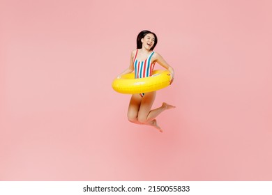 FUll body young woman of Asian ethnicity in striped one-piece swimsuit hawaii lei yellow inflatable ring jump high into water isolated on plain pastel pink background. Summer vacation sea rest concept