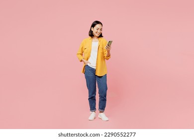 Full body young woman of Asian ethnicity wear yellow shirt white t-shirt stand hold in hand use mobile cell phone chatting browsing internet isolated on plain pastel pink background studio portrait - Powered by Shutterstock