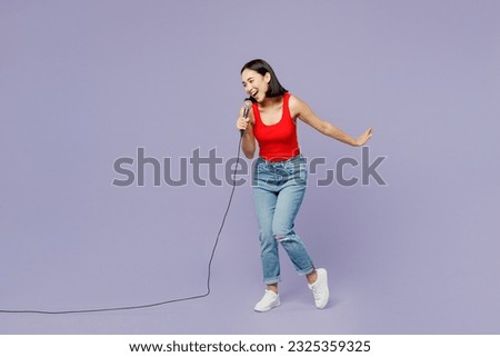 Full body young woman of Asian ethnicity wear casual clothes red tank shirt sing song in microphone at karaoke club isolated on plain pastel light purple background studio portrait. Lifestyle concept
