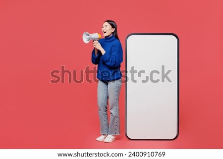 Full body young woman of Asian ethnicity she wear blue sweater casual clothes big huge blank screen mobile cell phone smartphone with area scream in megaphone isolated on plain pastel light background