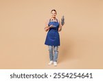 Full body young woman barista bartender barman employee wear blue apron shirt work in coffee shop hold shaker make alcohol cocktail isolated on plain beige background. Small business startup concept