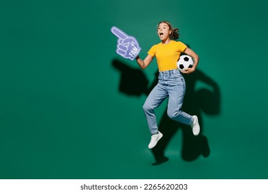 Full body young woman fan wear yellow t-shirt foam 1 glove finger up point overhead cheer up support football sport team hold in hand soccer ball watch tv live stream isolated on dark green background - Powered by Shutterstock