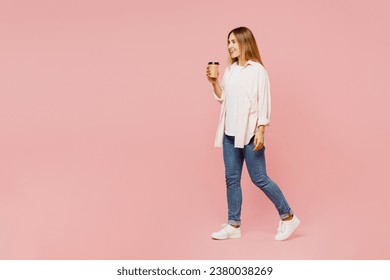 Full body young woman she wear shirt white t-shirt casual clothes hold takeaway delivery craft paper brown cup coffee to go isolated on plain pastel pink background studio portrait. Lifestyle concept